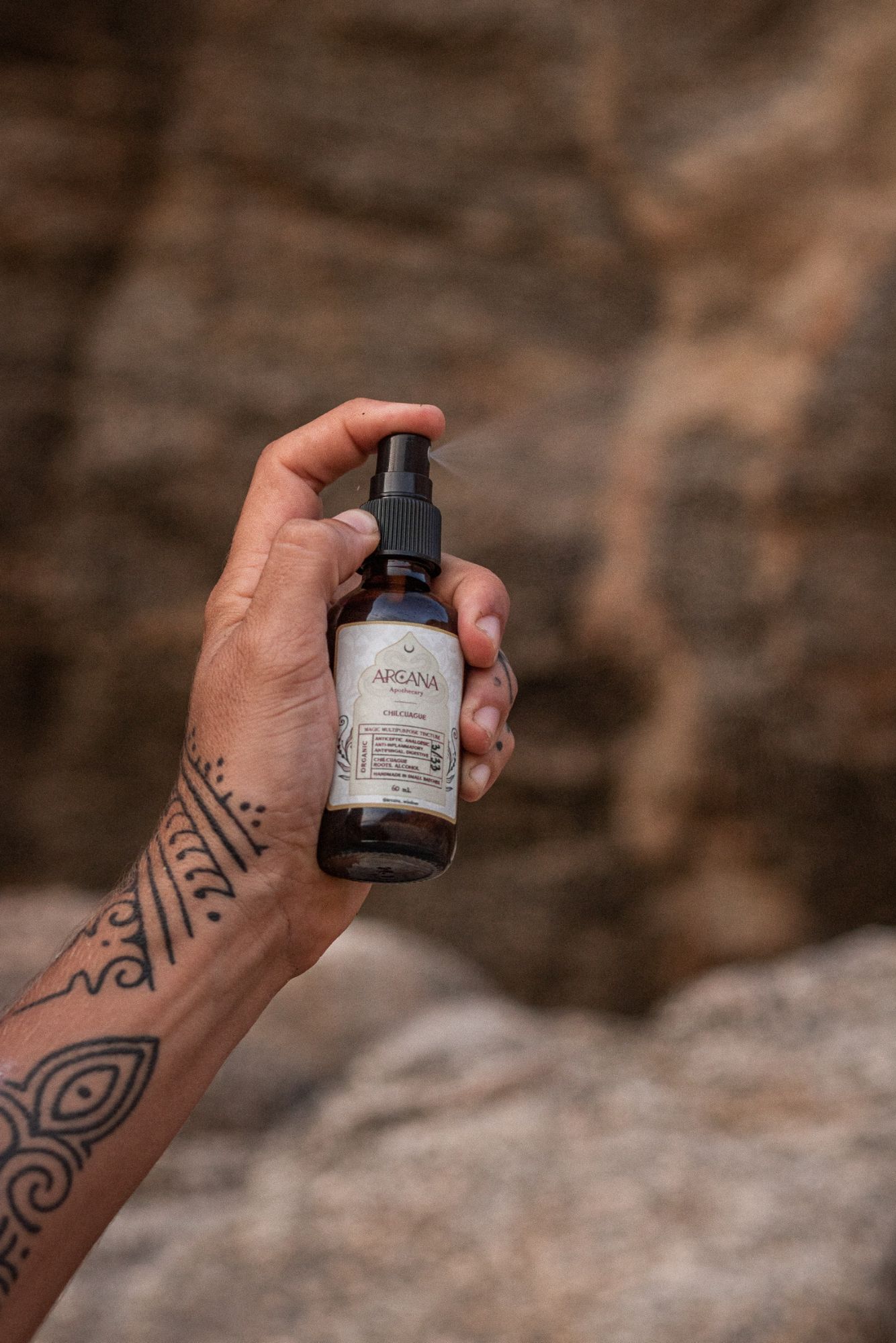 Tattooed hand misting the ARCANA Chilcuague spray against stone