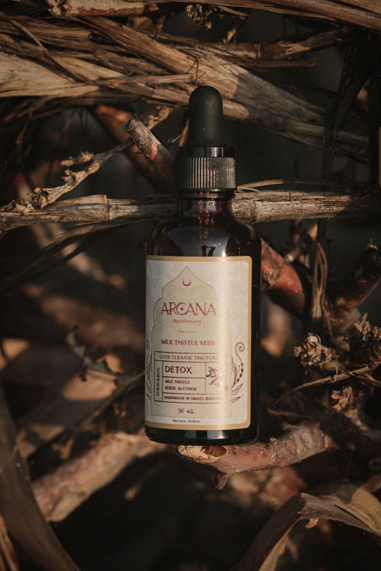 ARCANA Milk Thistle tincture bottle resting among dry branches