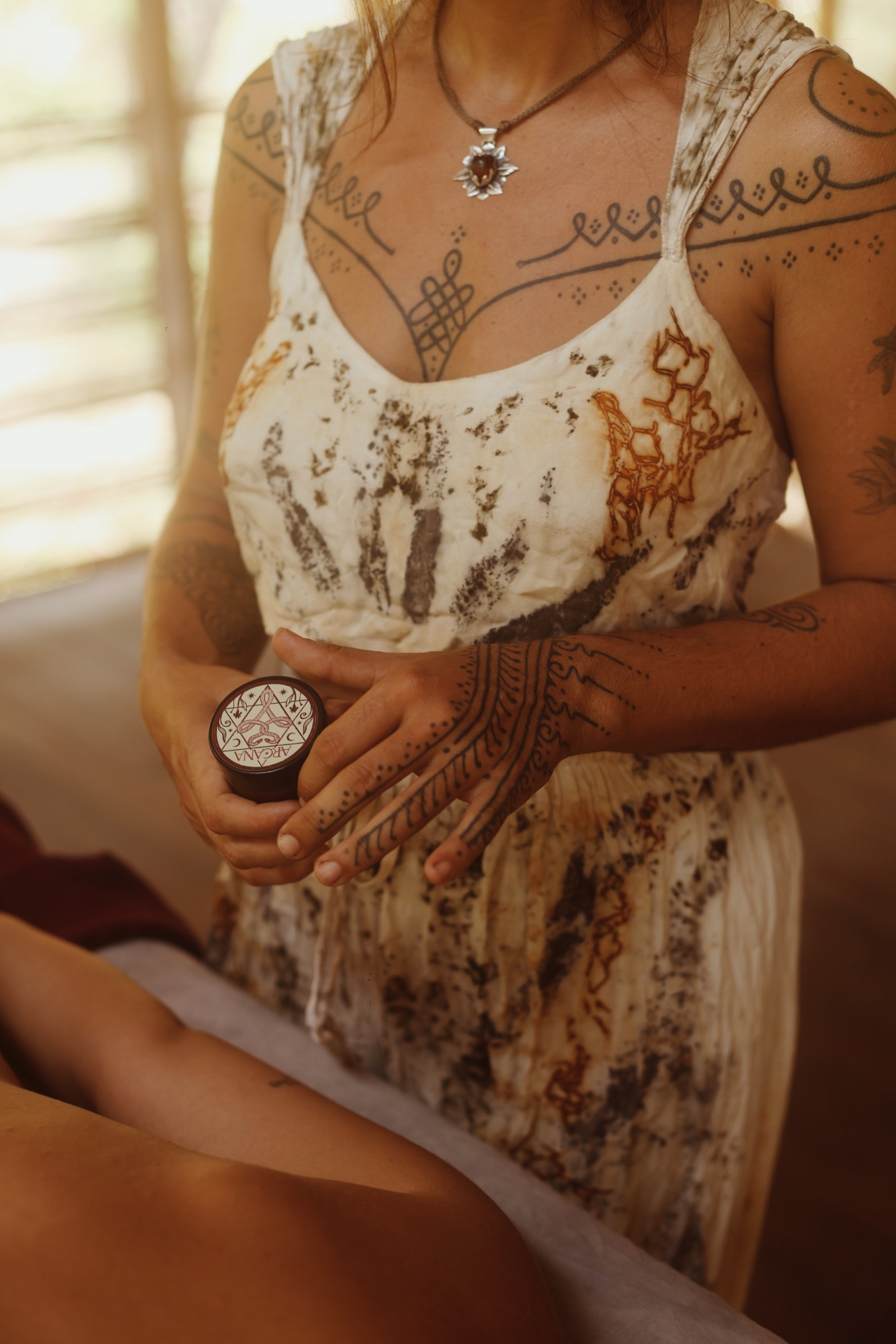 Hands holding the ARCANA ointment jar with its emblem lid